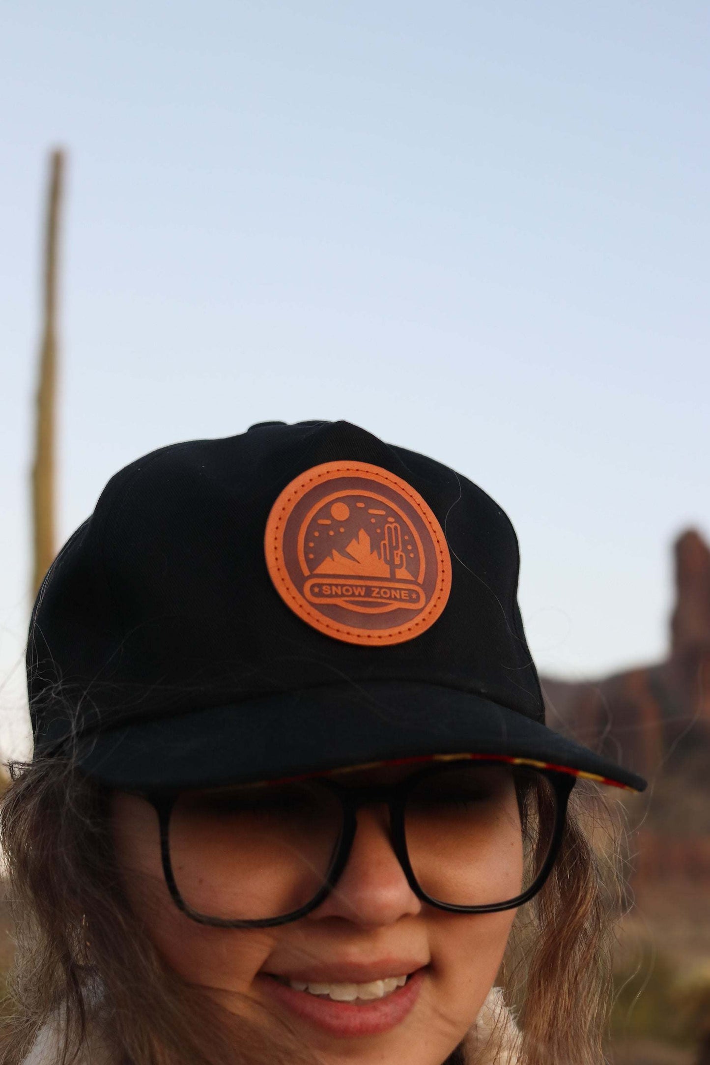 Black 5 panel hat with a leather patch worn by a person outdoors