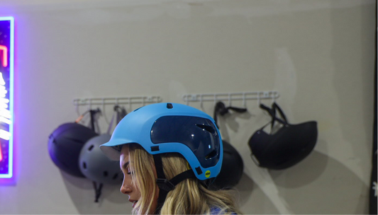 Woman wearing a blue helmet for helmet rental with other helmets hanging on the wall in the background