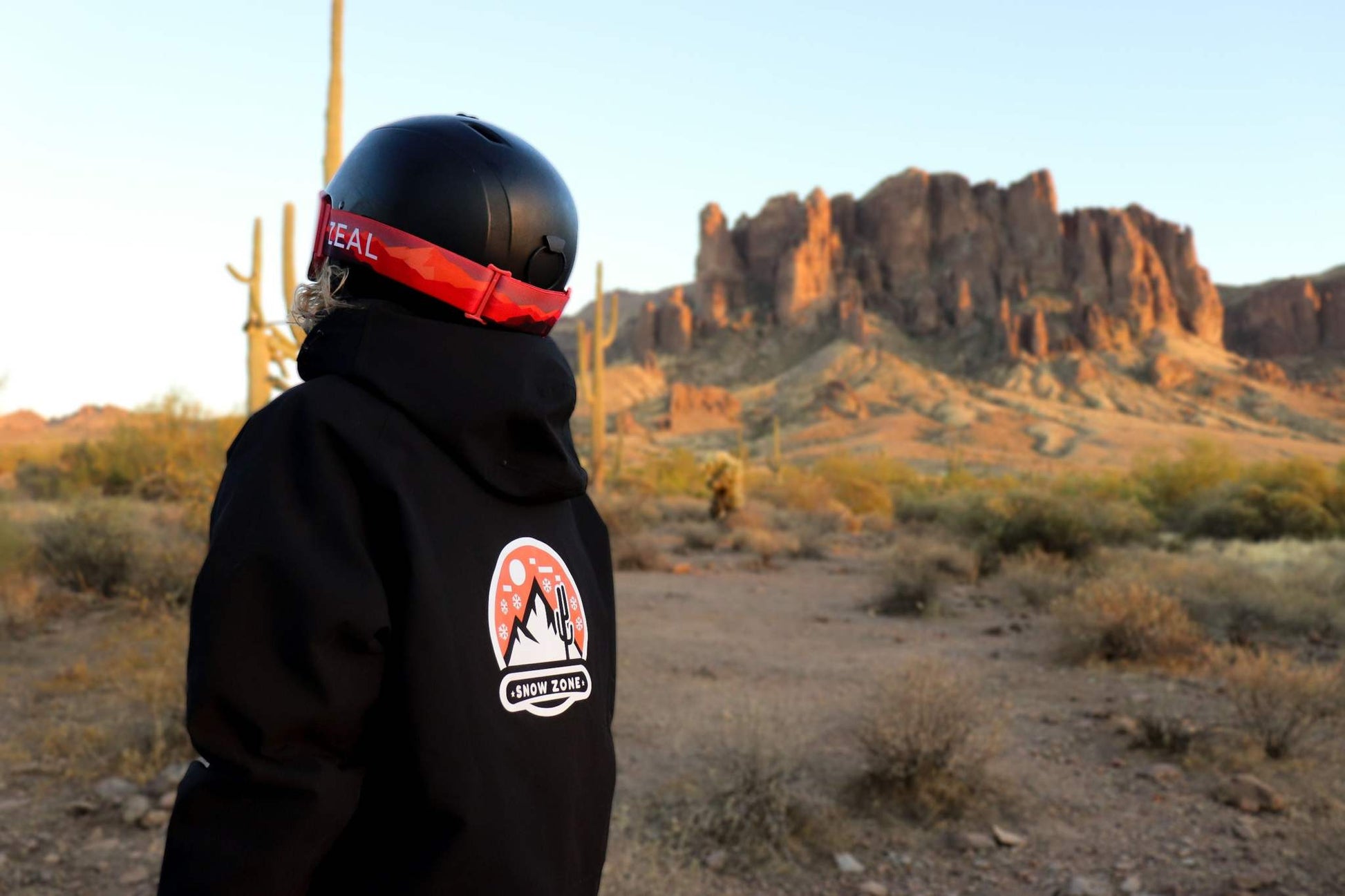 Person wearing black insulated snow jacket with a helmet in a desert landscape with rocky mountains in the background
