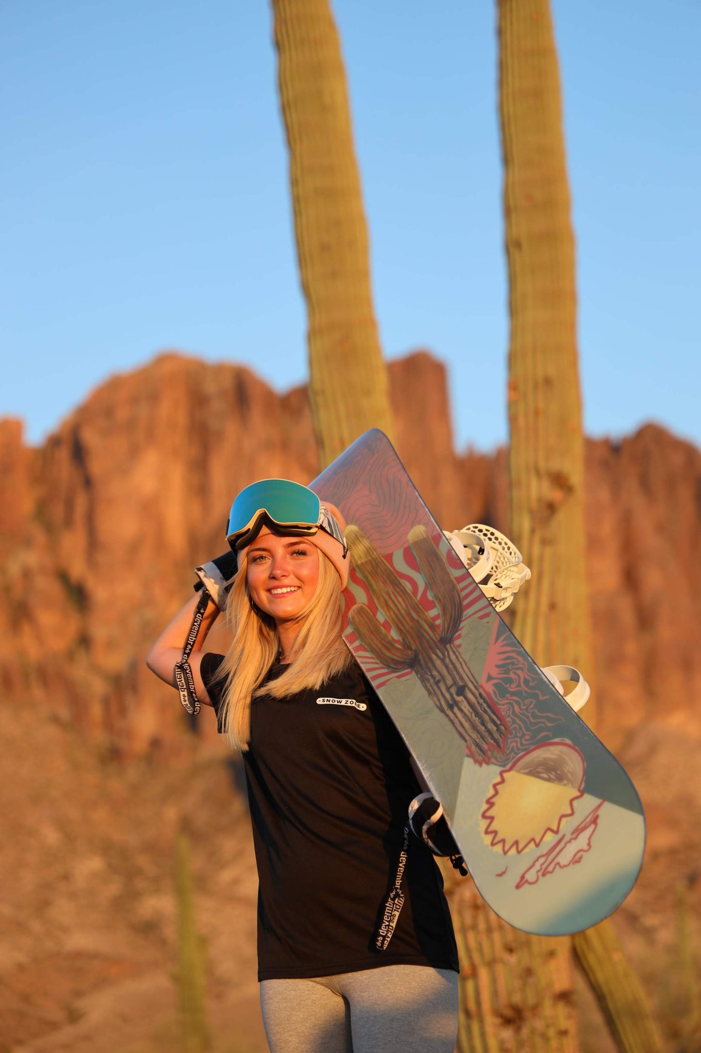 Woman wearing black dry fit short sleeve shirt holding snowboard in desert landscape