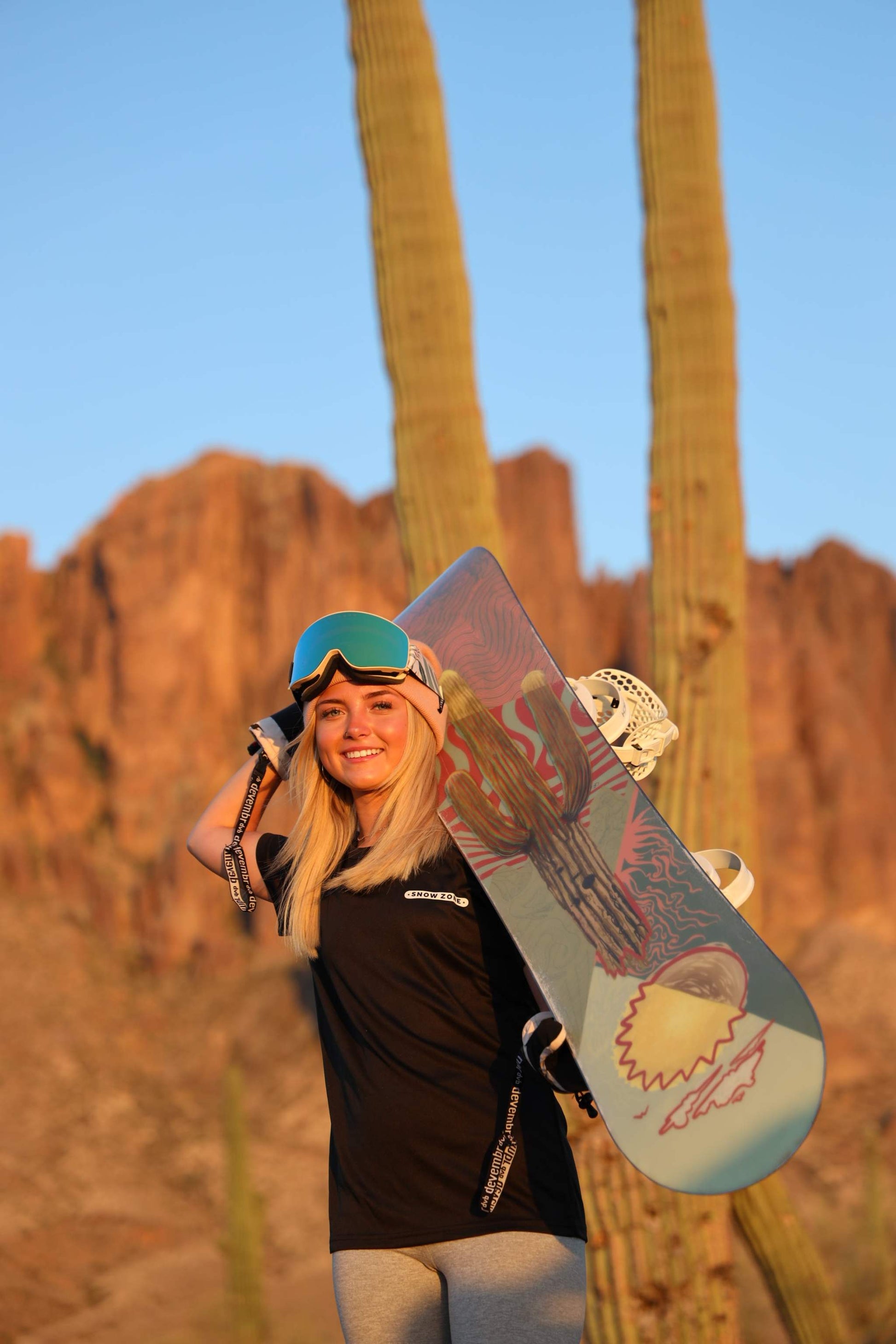 Woman wearing black dry fit short sleeve shirt holding snowboard in desert landscape