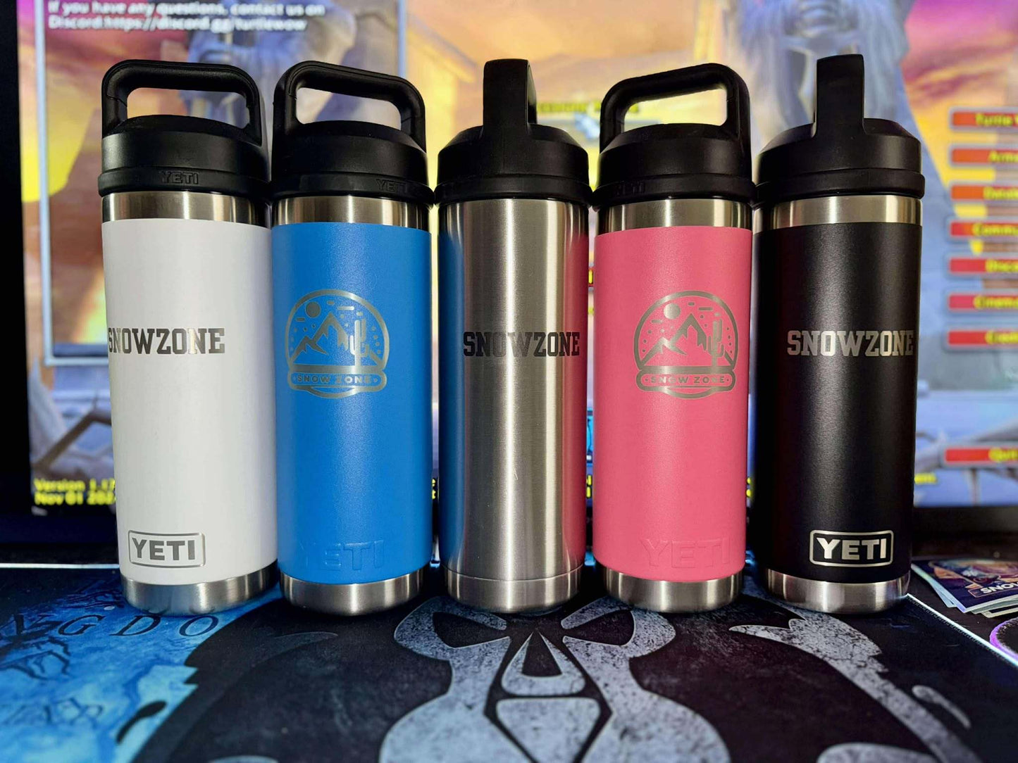 Five 18 oz Yeti Bottles with chug caps in white, blue, stainless steel, pink, and black colors displayed on a table.