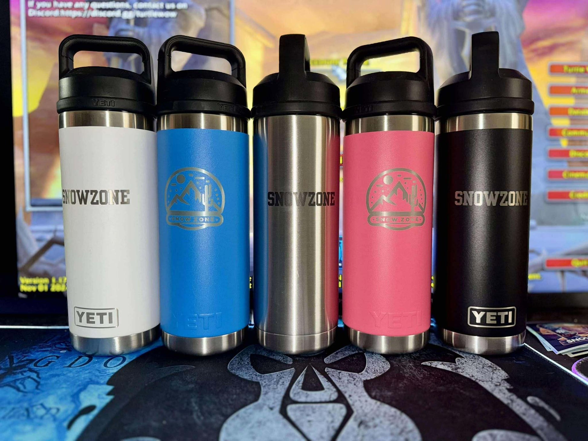 Five 18 oz Yeti Bottles with chug caps in white, blue, stainless steel, pink, and black colors displayed on a table.