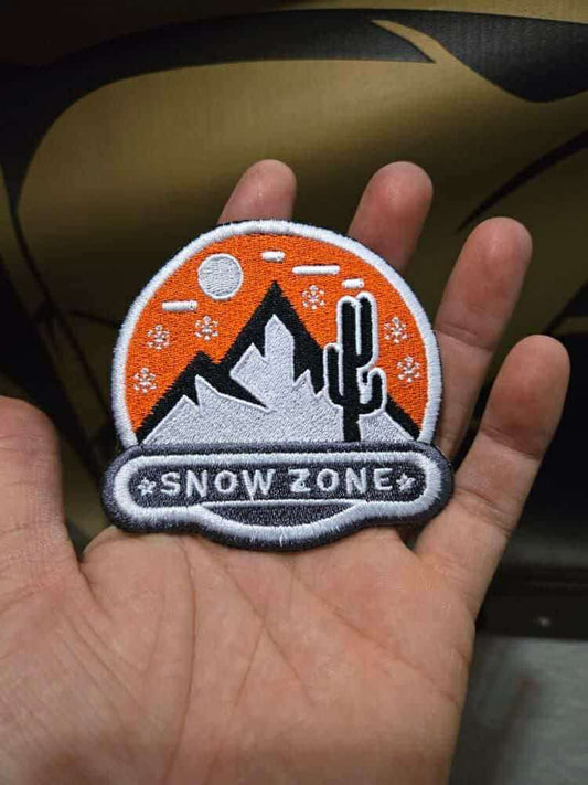 Hand holding embroidered patch with mountain, cactus, moon, and "Snow Zone" text design