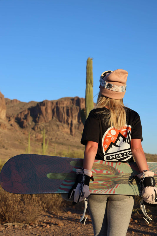 Woman wearing black dry fit short sleeve shirt holding snowboard in desert landscape