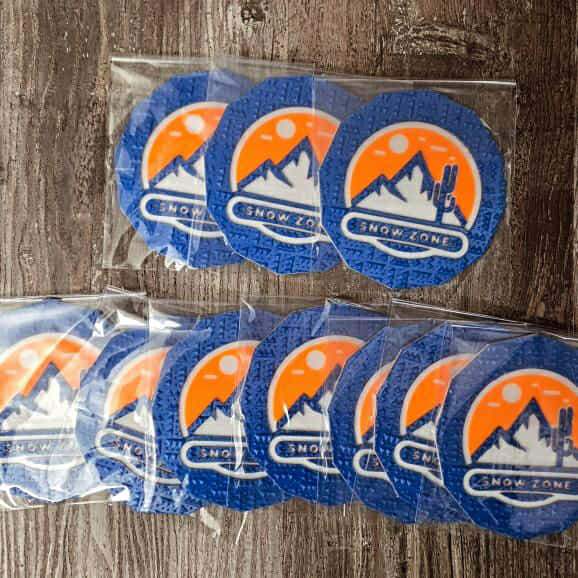 Blue and orange Snow Zone stomp pads by Sticky_ride in individual plastic bags on wooden surface
